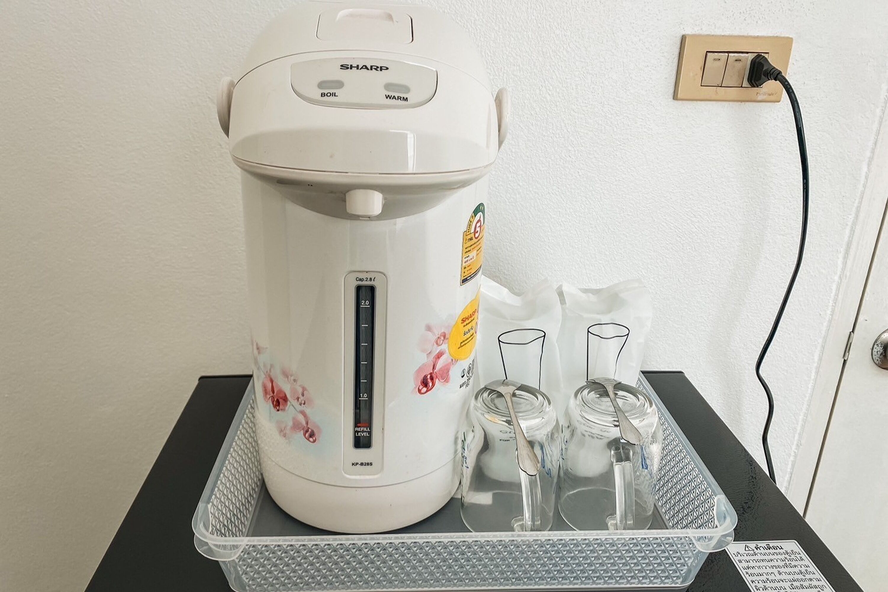 A white Sharp electric kettle with floral designs, a power cord, and two glass containers on a black tray.