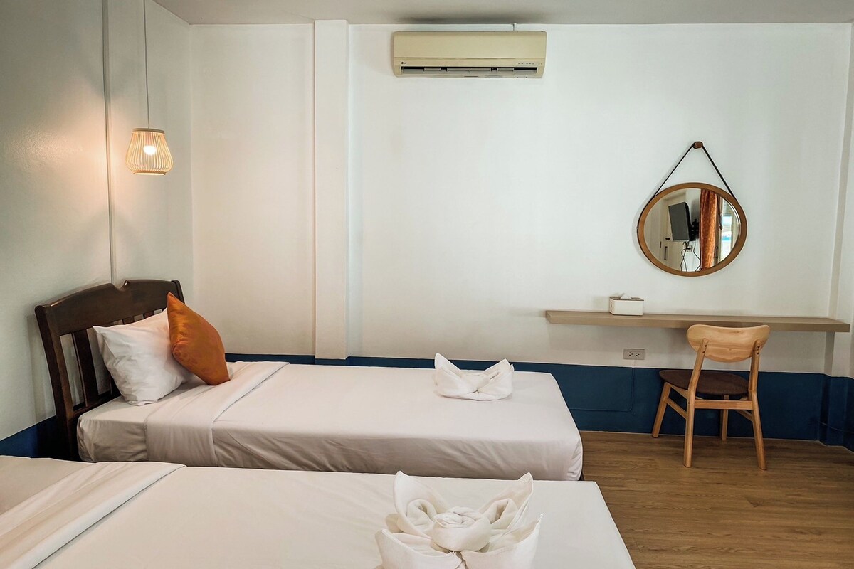 A hotel room with two beds, a desk, a chair, a mirror, and an air conditioning unit.