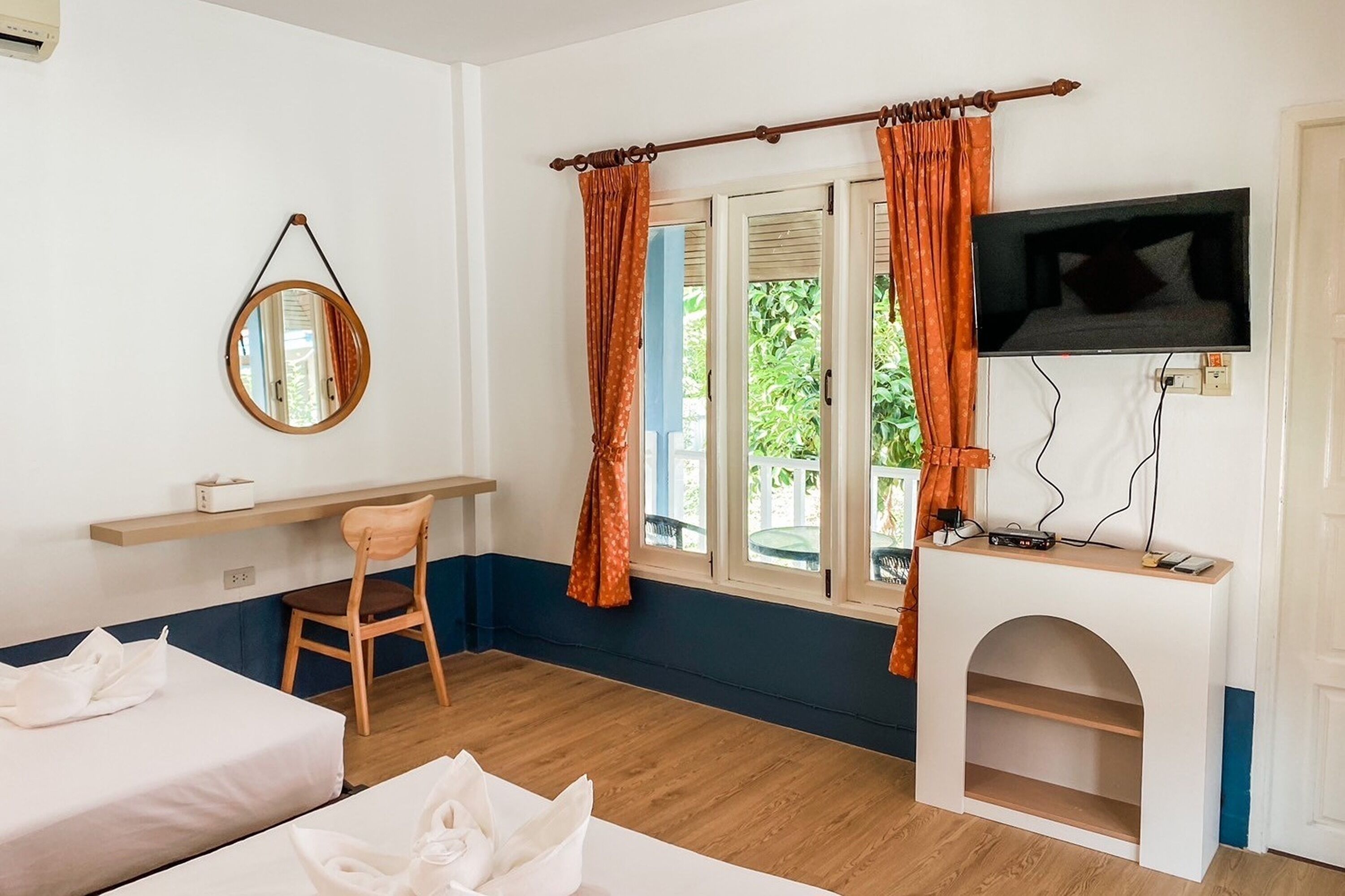 Habitación de hotel con dos camas, un televisor en un mueble, un espejo en la pared y una ventana con cortinas.