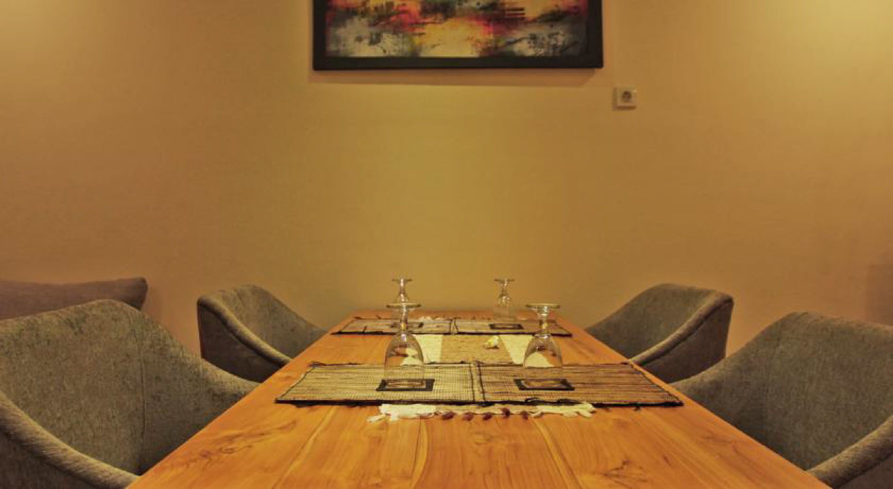 Una larga mesa de madera con cuatro sillas, cada una con un candelabro, frente a una pared lisa con una obra de arte enmarcada en la parte superior.