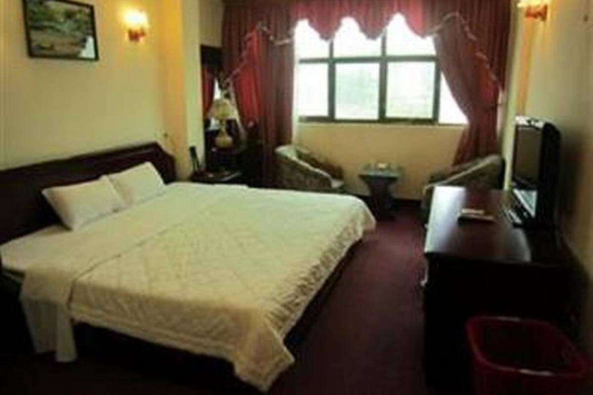 Ein Hotelzimmer mit Bett, Schreibtisch, Stuhl, Fernseher und einem Fenster mit Vorhängen.