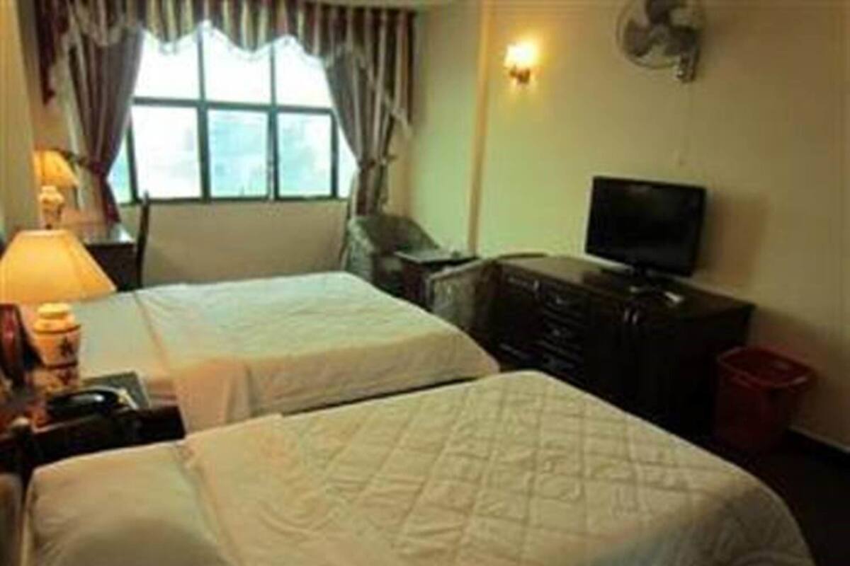 Ein Hotelzimmer mit zwei Betten, einem Fernseher, einem Schminktisch und einem Fenster mit Vorhängen.