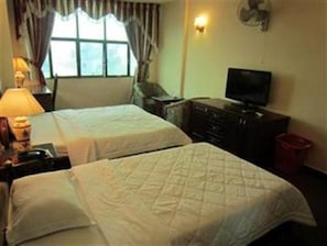 Een hotelkamer met twee bedden, een televisie, een dressoir en een raam met gordijnen.