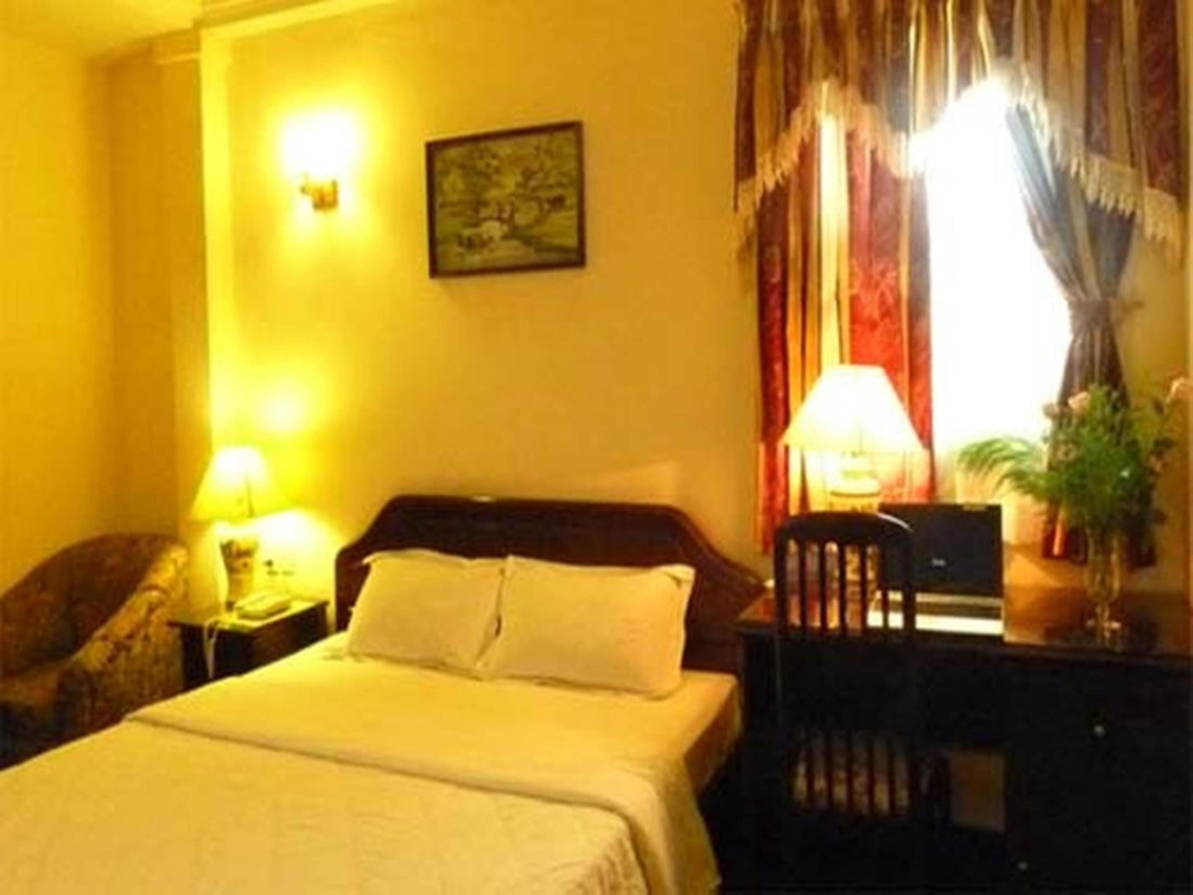 Habitación de hotel con cama, escritorio, silla, lámpara, un cuadro en la pared y ventana con cortinas.