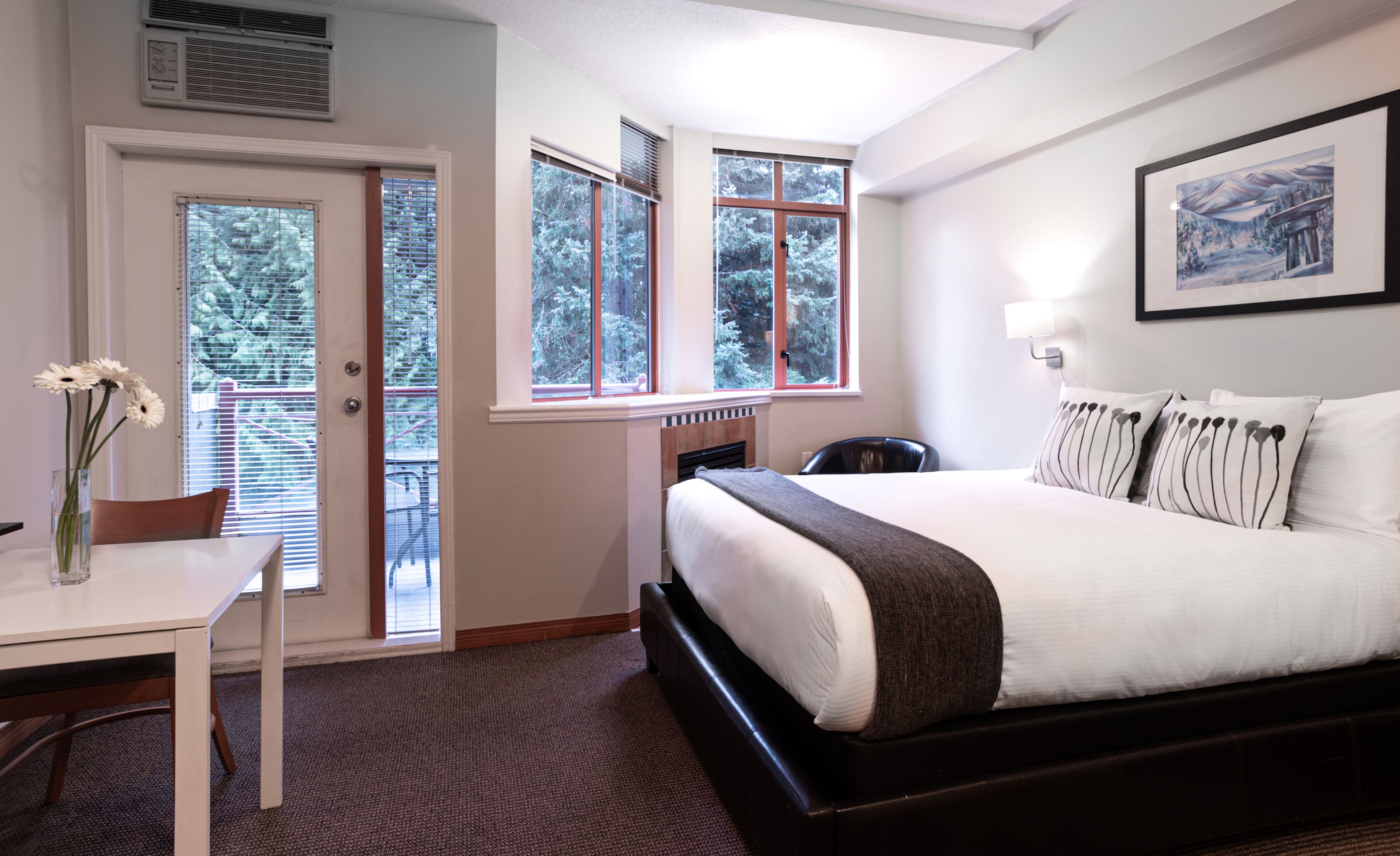 Ein Hotelzimmer mit Bett, Schreibtisch, Stuhl und einem Fenster mit Blick auf Bäume.