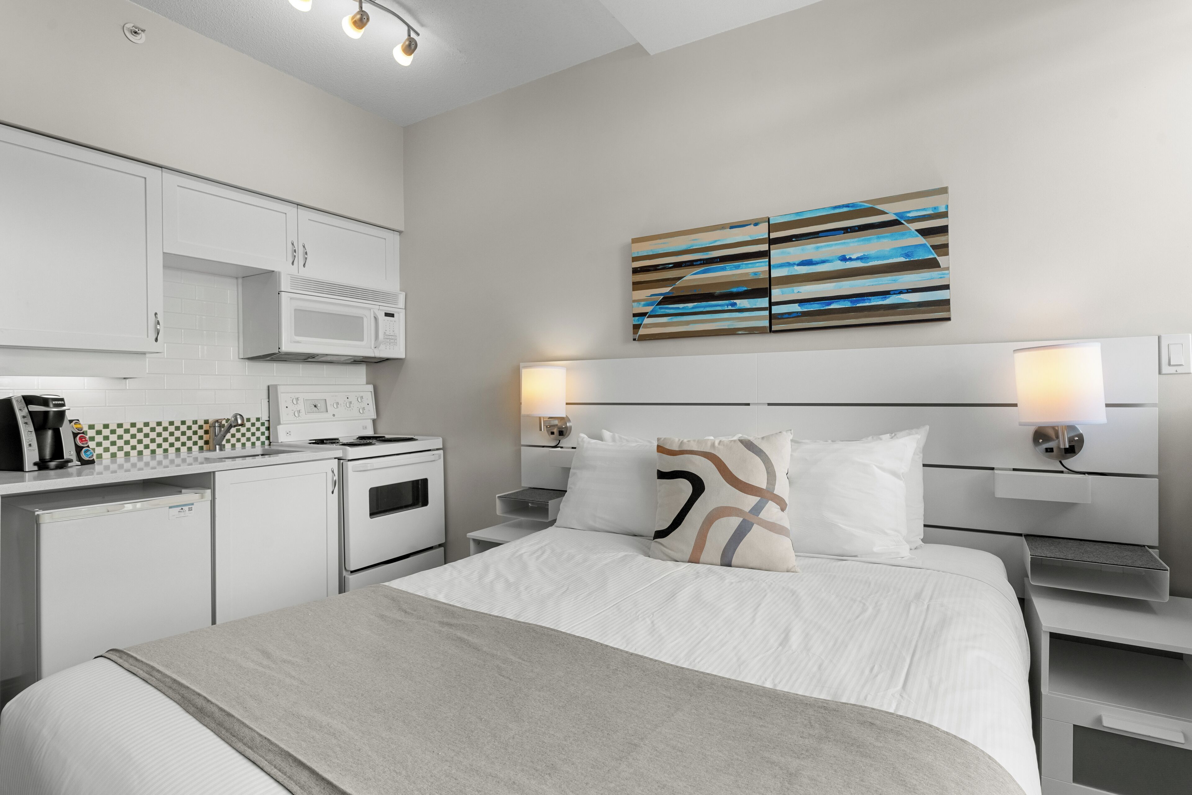 Een moderne hotelkamer met een bed, nachtkastjes, een magnetron en een kleine kitchenette.
