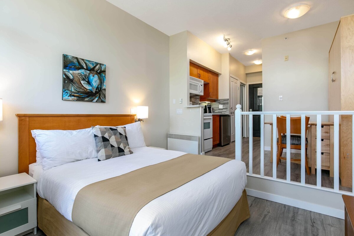 Una habitación de hotel con cama, un cuadro, una kitchenette y un área de comedor.