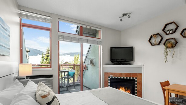 A hotel room with a bed, a television, a fireplace, and a balcony with a view of the mountains. - Alpenglow Lodge by MountainView (Whistler)