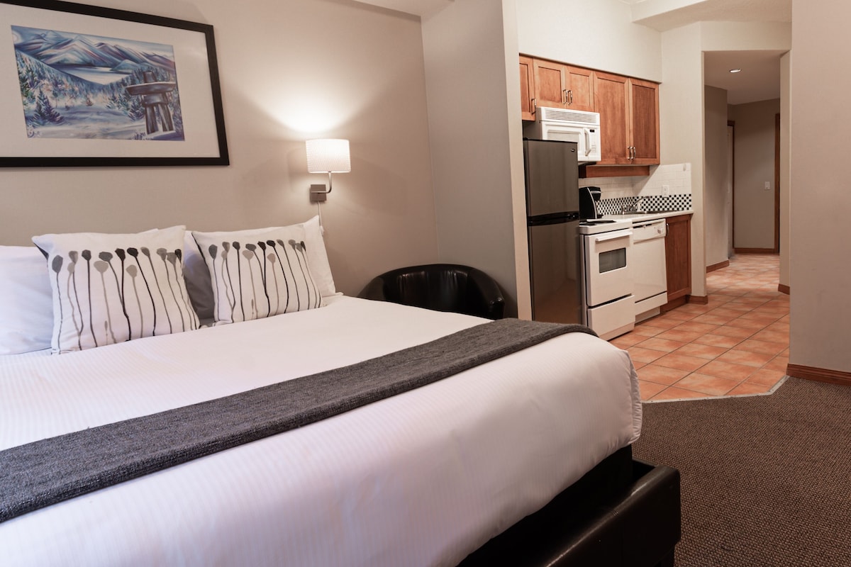 Una habitación de hotel con una cama, un escritorio, una silla, un refrigerador y un microondas.