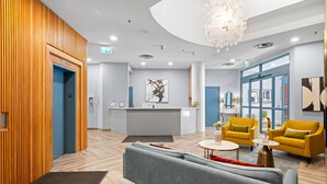 A modern lobby with a reception desk, a grey sofa, yellow armchairs, and a wooden wall. - Alpenglow Lodge by MountainView (Whistler)