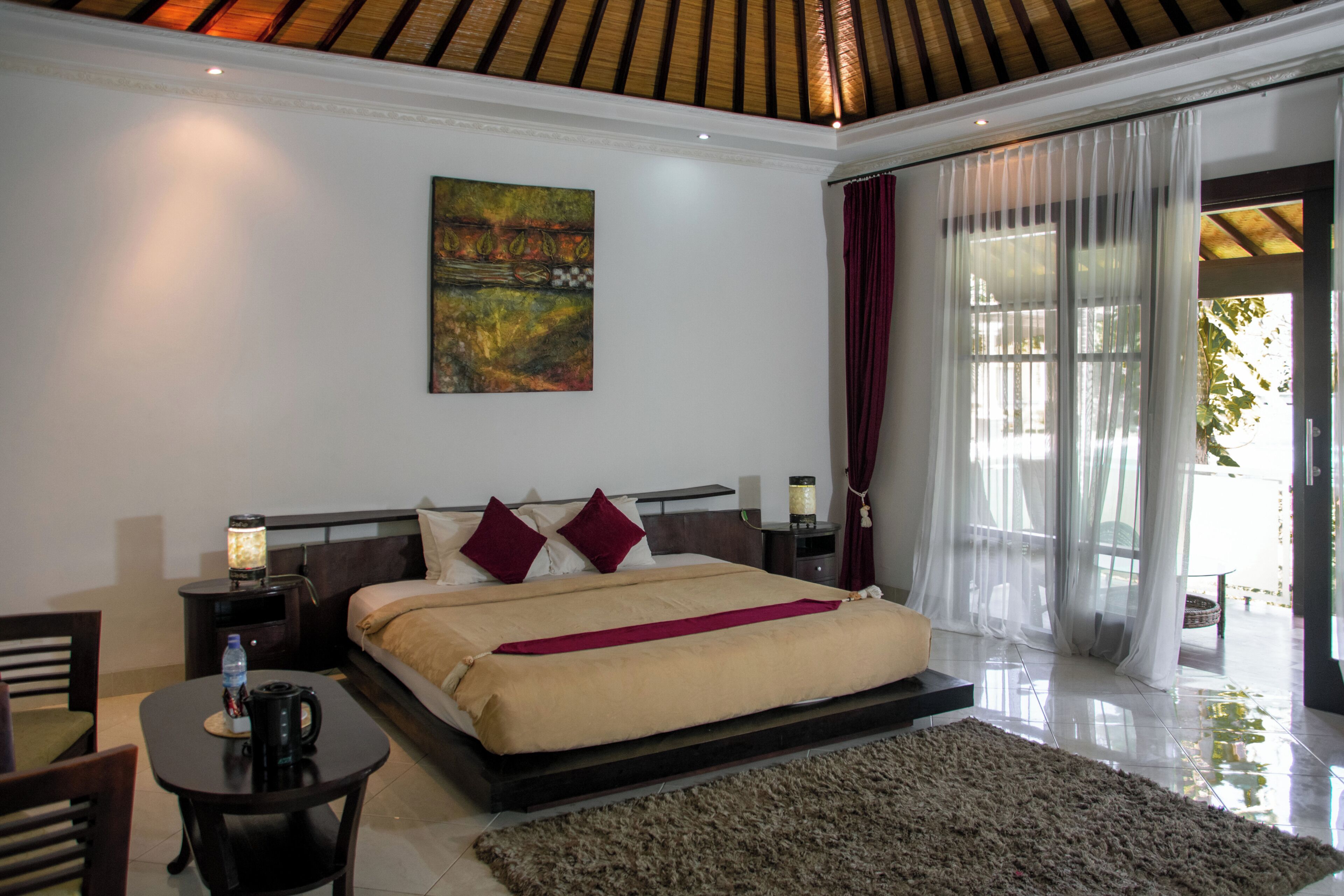 A bedroom with a bed, bedside tables, a nightstand, a coffee table, and a view of the outdoors.