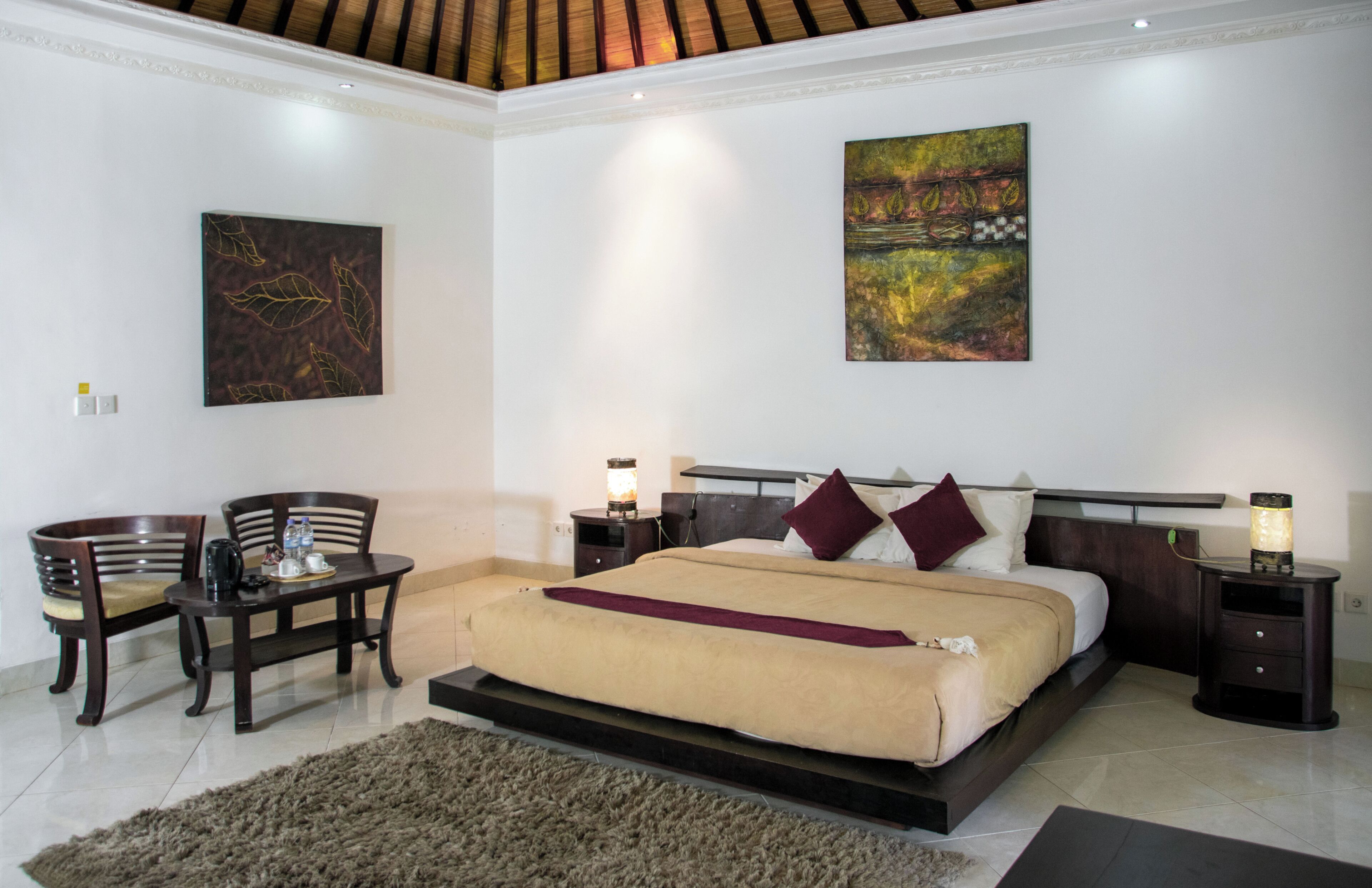 A bedroom with a bed, two nightstands, a table with chairs, and two paintings on the walls.