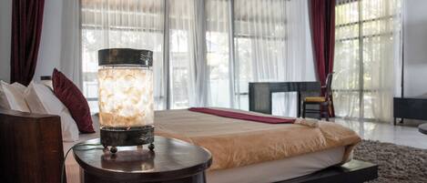 A modern bedroom with a large bed, a bedside table with a lamp, and a view of the outdoors through sheer curtains.