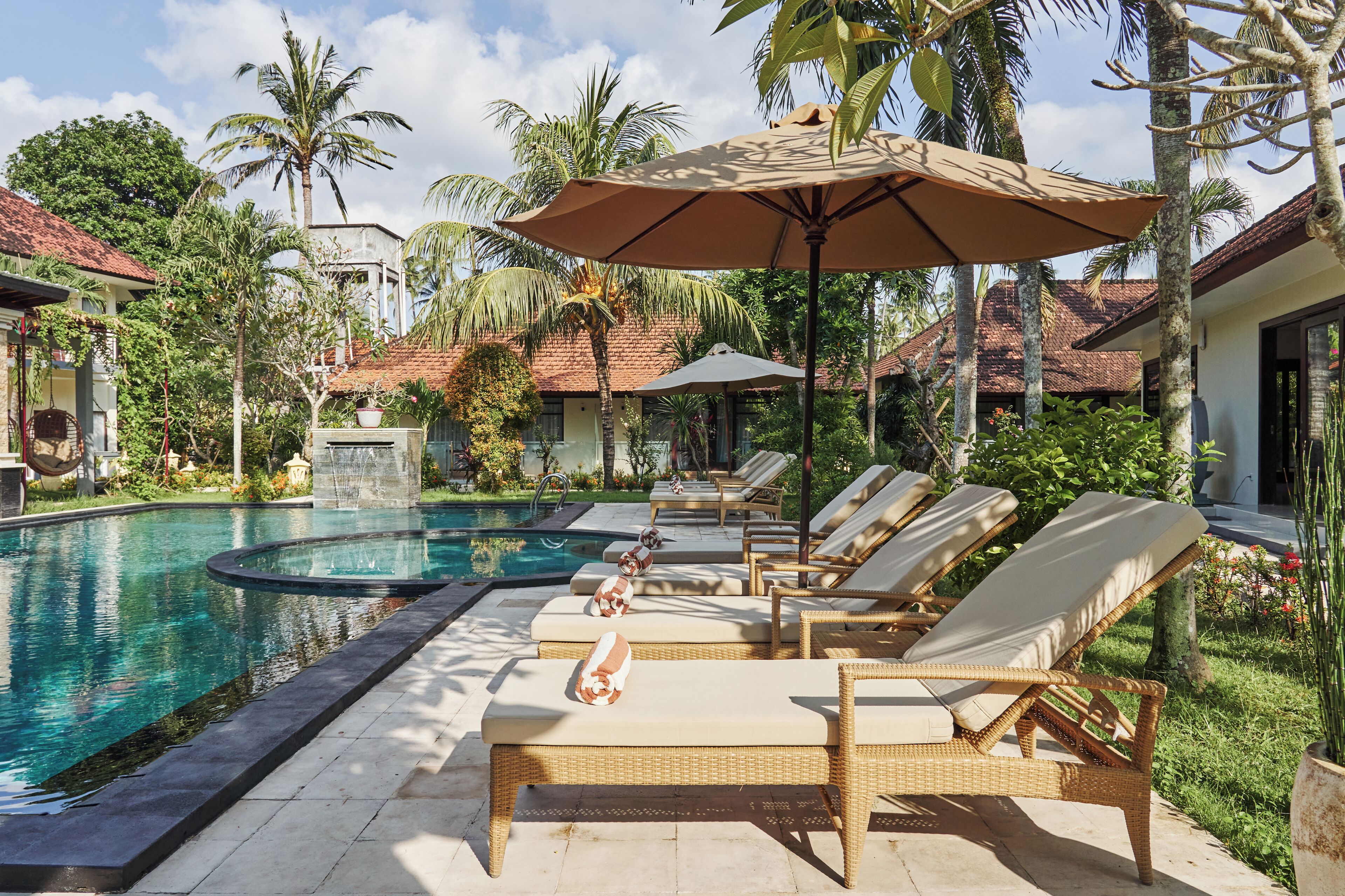 Zona de piscina con sillas de descanso, una sombrilla y un jardín tropical.