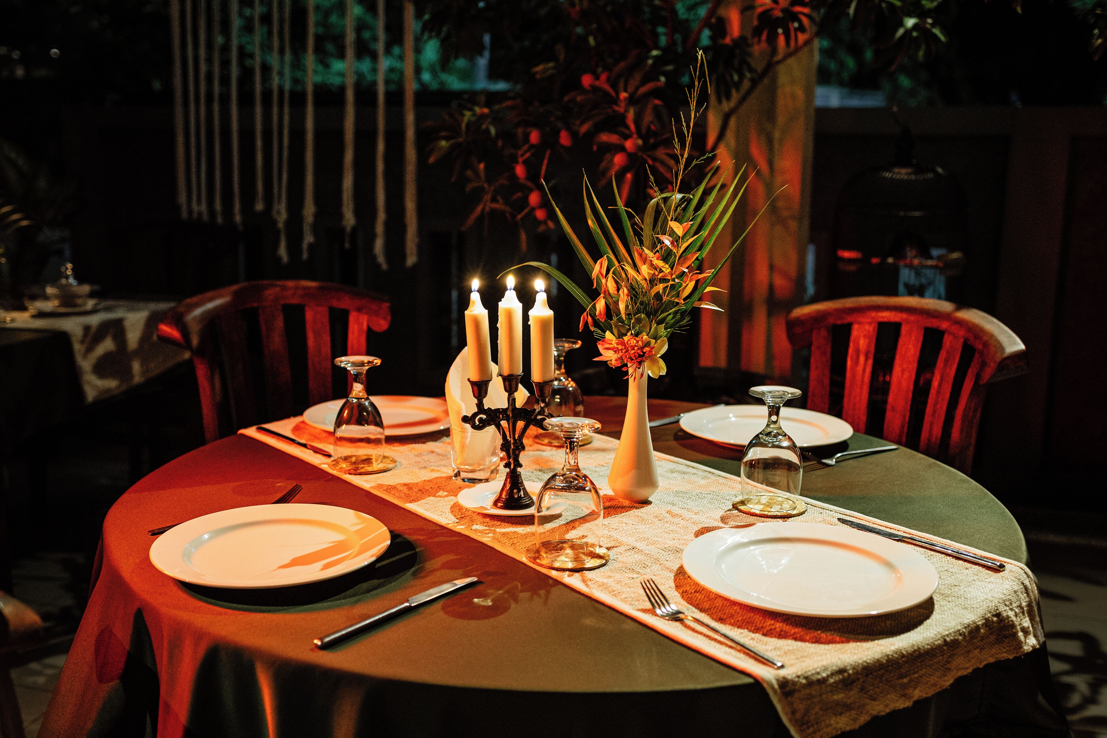 A dining table set with plates, cutlery, candles, and a vase of flowers.