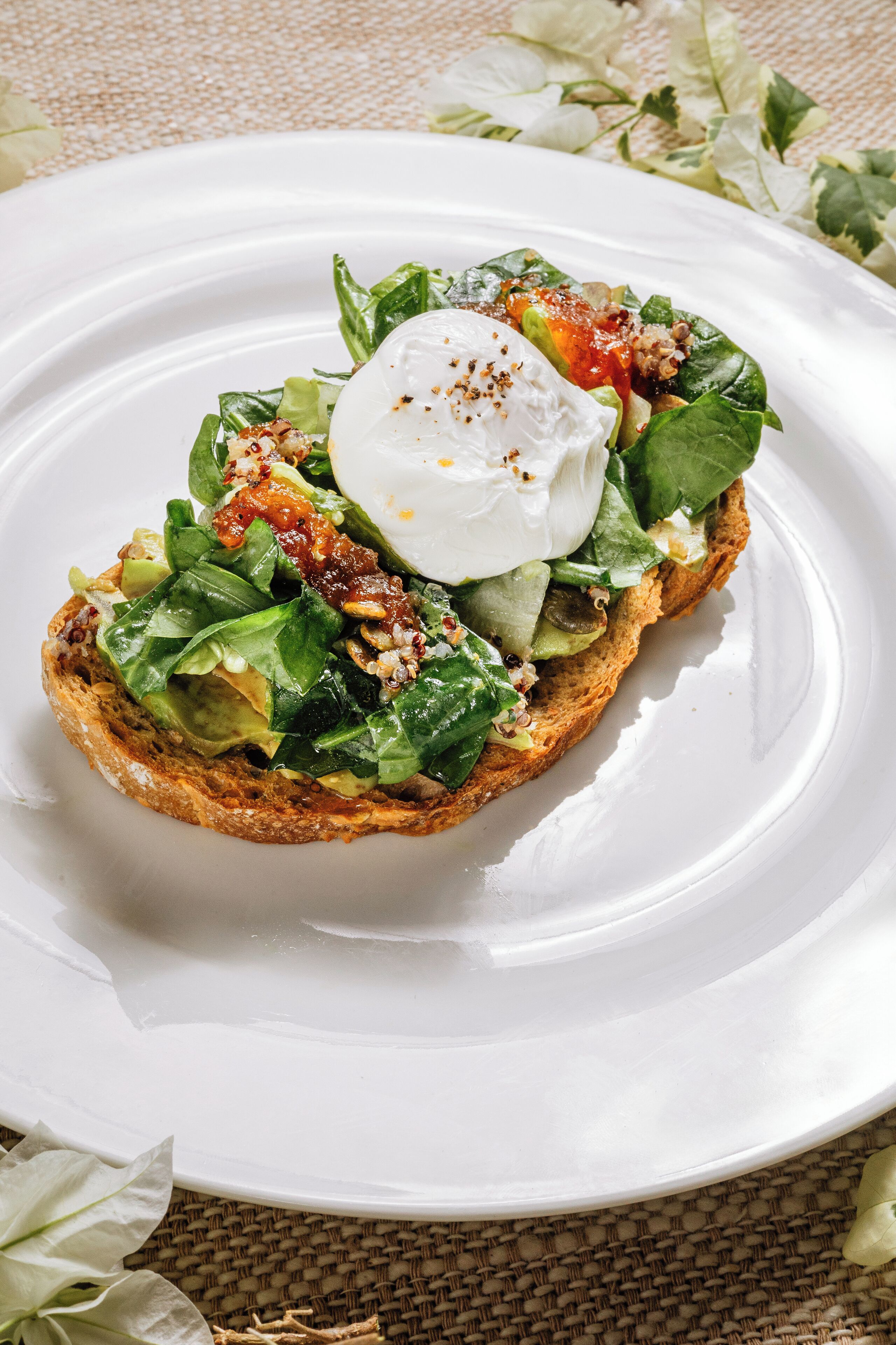 Une assiette contenant un sandwich garni de légumes verts, d’un œuf poché et d’une sauce rouge.