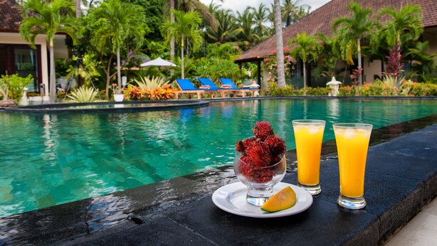 A poolside view with a glass of juice, a bowl of fruit, and lounge chairs.