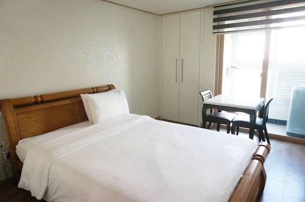 Une chambre d’hôtel avec un lit en bois, une petite table et des chaises, ainsi qu’une fenêtre avec des stores.
