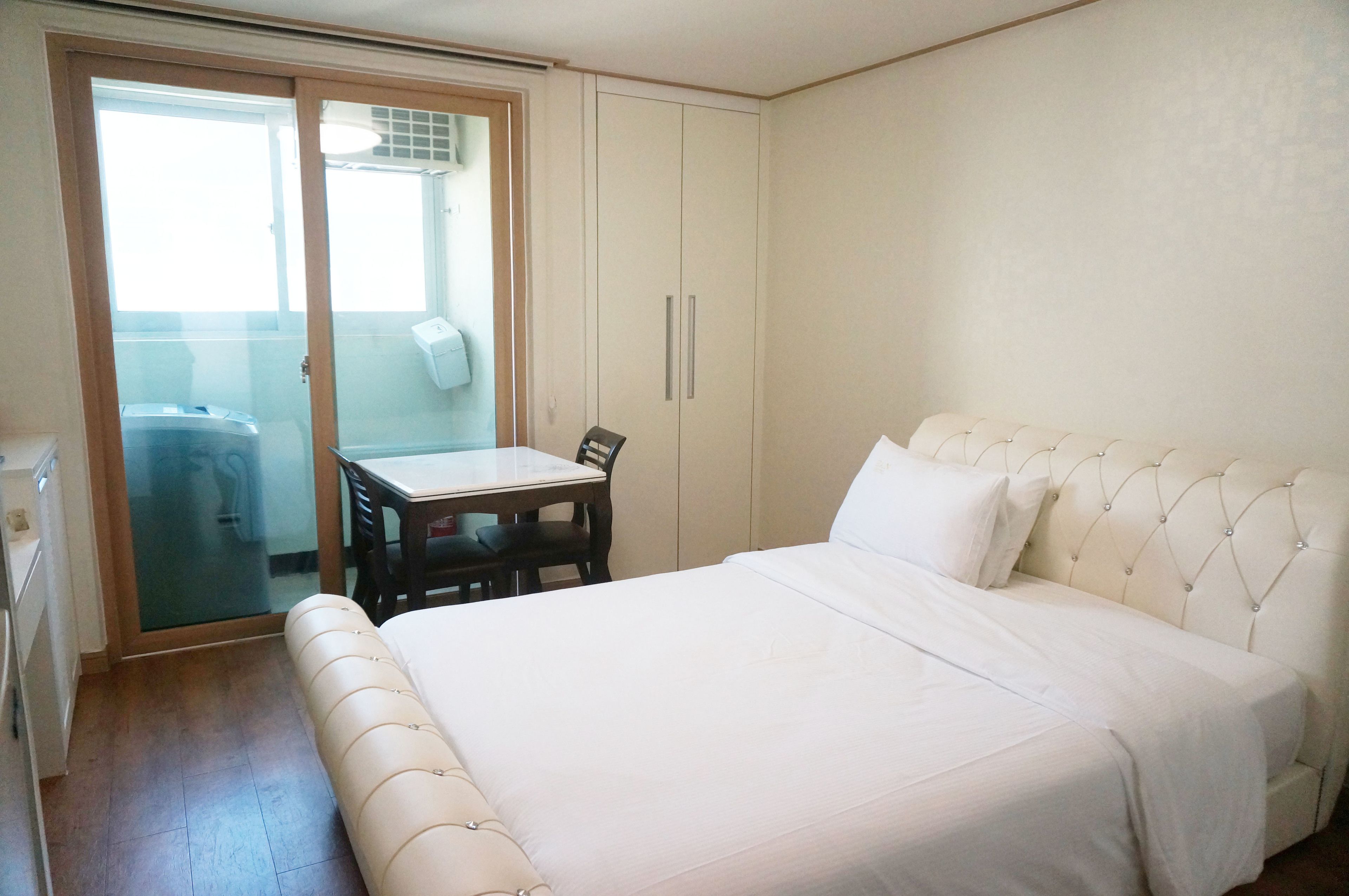 Een slaapkamer met een bed, een tafel en een stoel. Er is een schuifdeur die leidt naar een balkon.