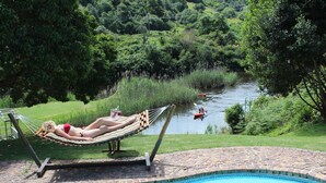 Zona de piscina con una hamaca, vista a un río y borde de piedra alrededor de la piscina.