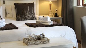 Una cama bien tendida con sábanas blancas, un cojín decorativo marrón oscuro y una bandeja con un vaso de agua y artículos de aseo.