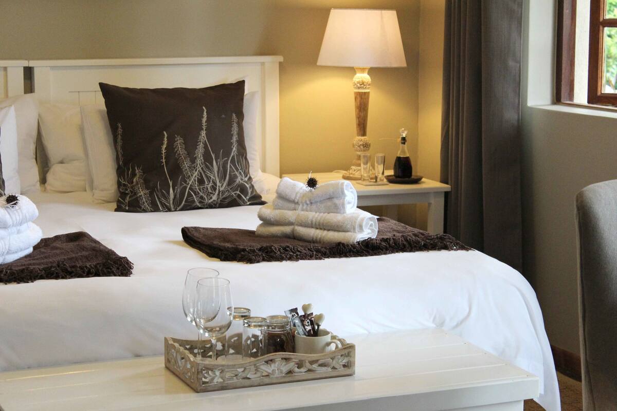 A neatly made bed with white linens, a dark brown decorative pillow, and a tray with a glass of water and toiletries.