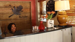 Un mostrador de recepción con un letrero de madera que dice "Blackwaters River Lodge", un reloj, un florero con flores y una lámpara.