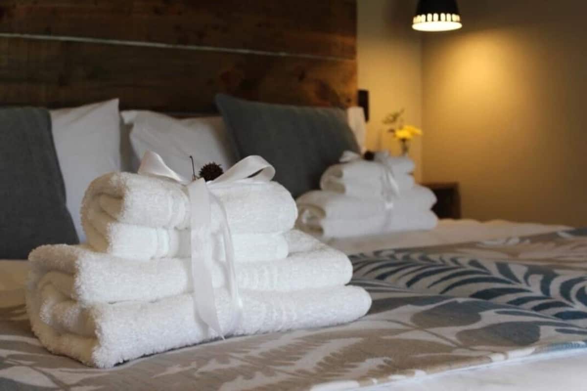 A neatly made bed with folded towels and pillows, a patterned bedspread, and a wooden headboard.