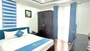Una habitación de hotel con cama, armario, escritorio y ventana con cortinas.