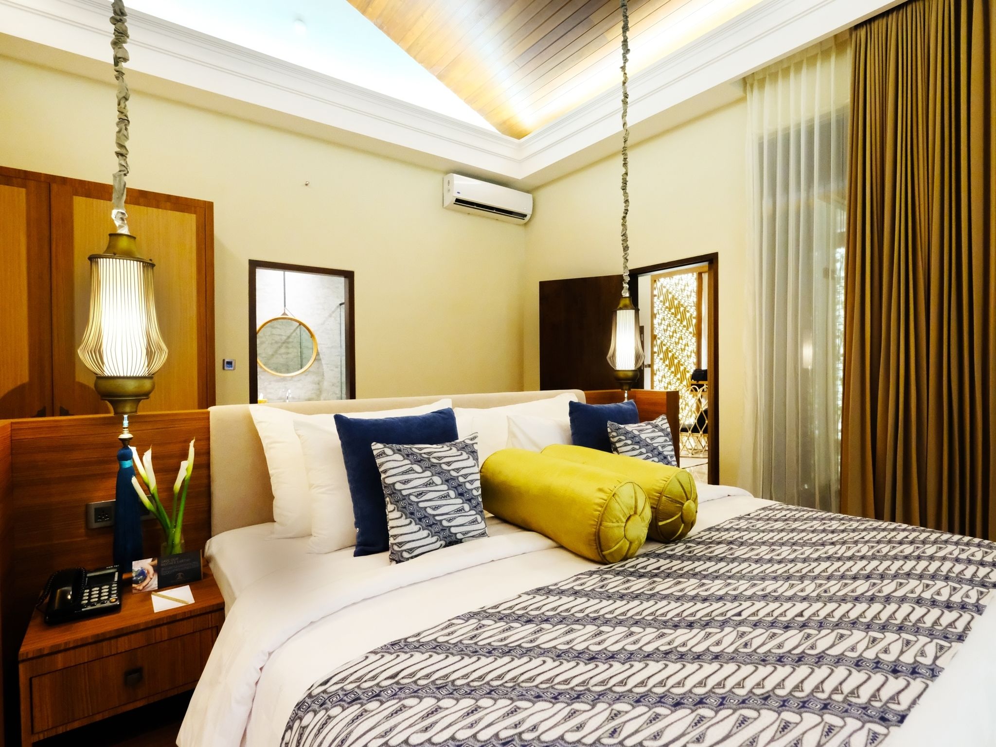 Une chambre d’hôtel comprenant un lit, des lampes de chevet, une table de chevet, un climatiseur fixé au mur et une fenêtre avec des rideaux.