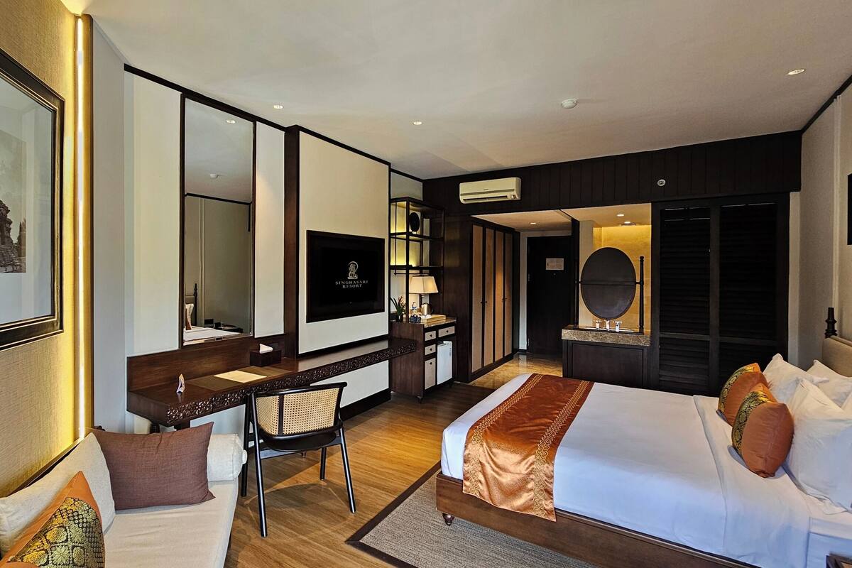 Ein modernes Hotelzimmer mit Bett, Schreibtisch, Stuhl, Fernseher, Spiegel und Kleiderschrank.