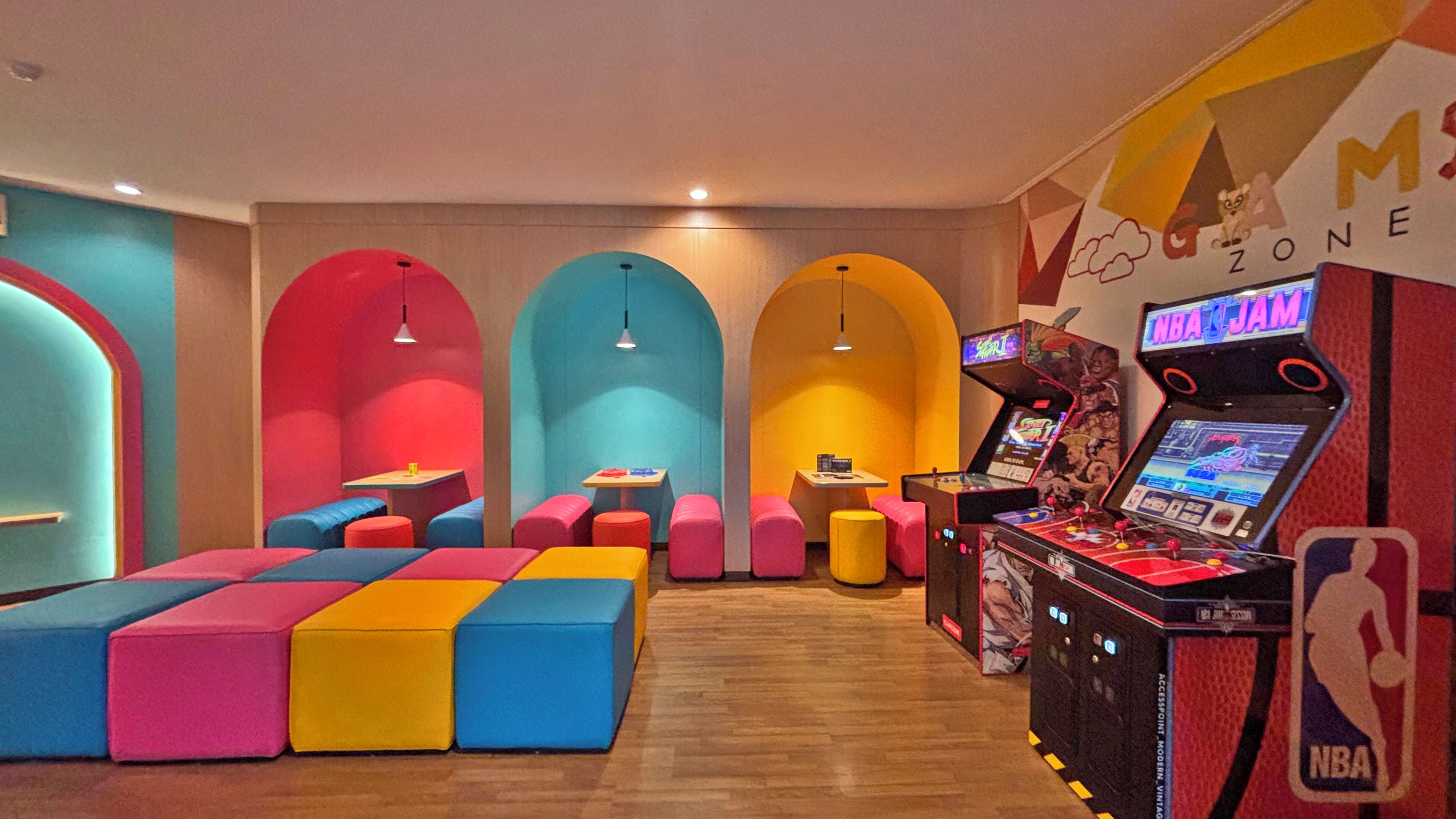 A brightly colored arcade area with seating and basketball arcade machines.