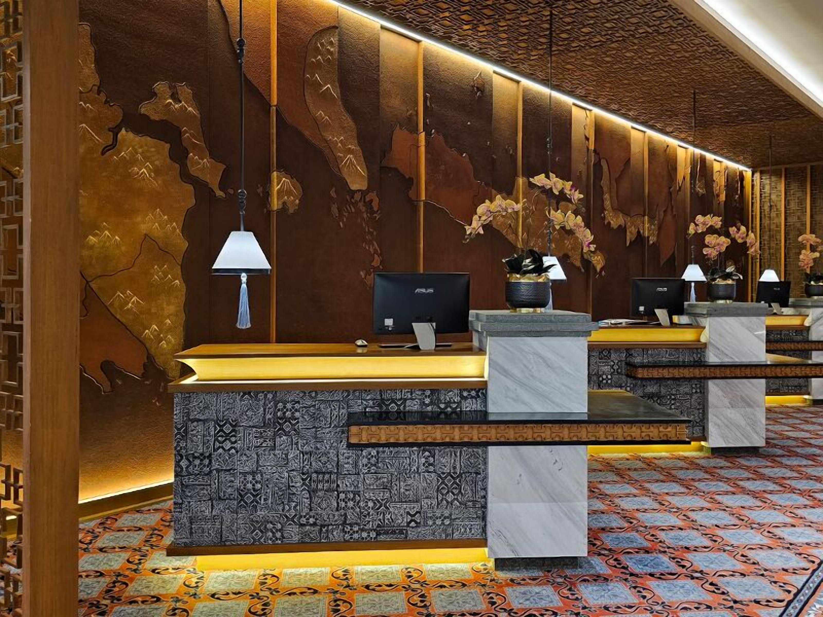 Un espace d’accueil d’hôtel avec un comptoir de réception en bois, plusieurs écrans d’ordinateur et un sol à motifs.