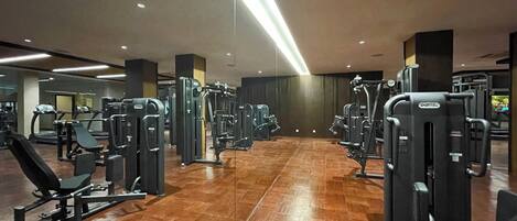 A gym with various exercise machines, wooden flooring, and a modern ceiling design.