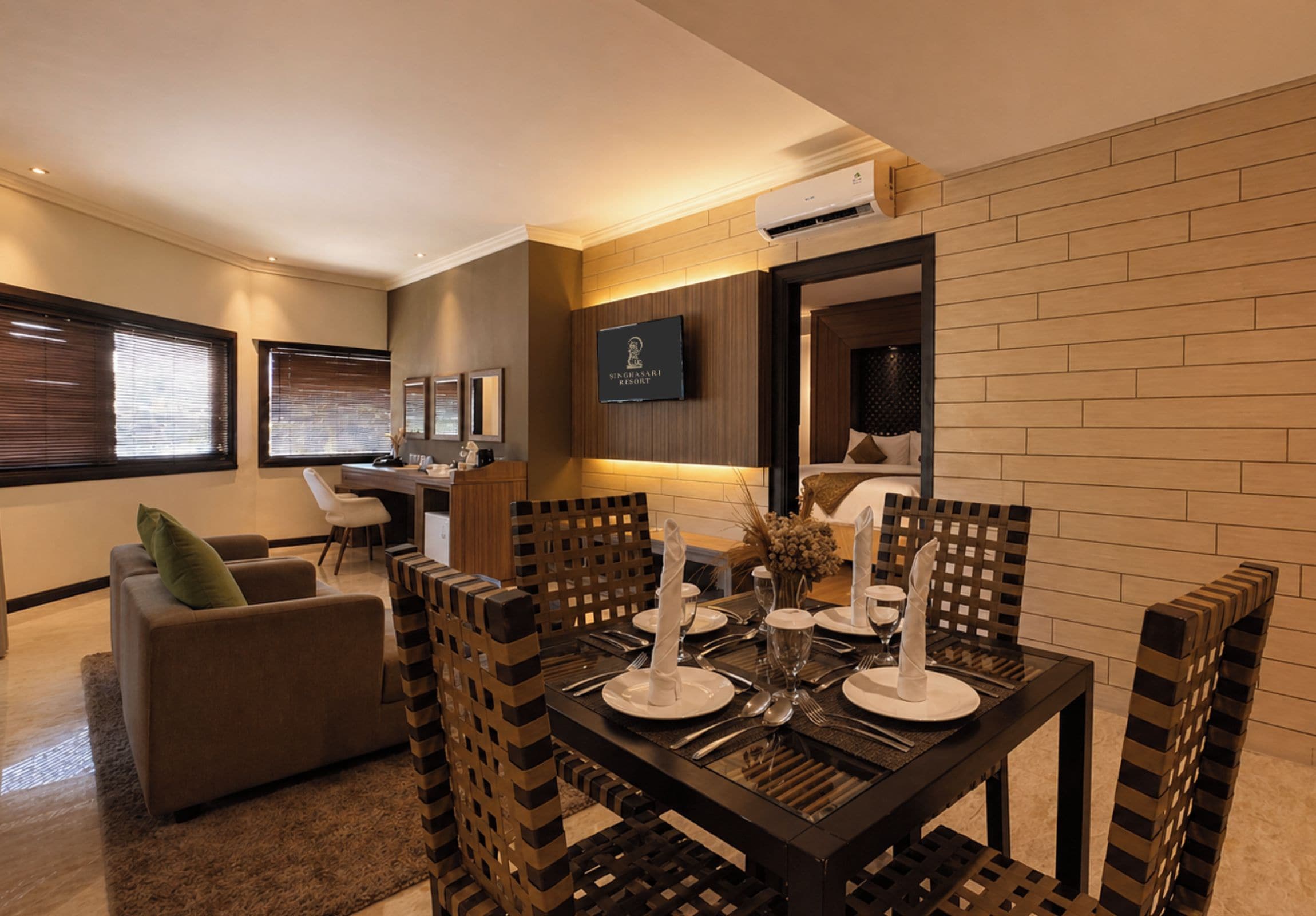 Un comedor moderno con una mesa de madera preparada para cuatro personas, un sofá y un televisor montado en la pared.