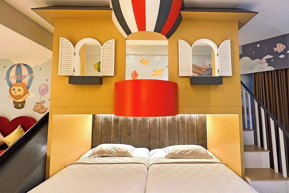 Ein Schlafzimmer mit einem Bett, einer roten Lampe und einer Wand mit Heißluftballon- und Tierabbildungen.