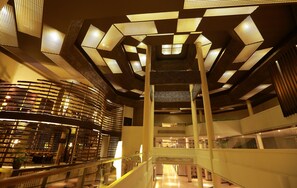 Un atrium à plusieurs niveaux, doté d’un escalier central, de rampes en verre et d’un plafond au design moderne agrémenté de motifs géométriques.