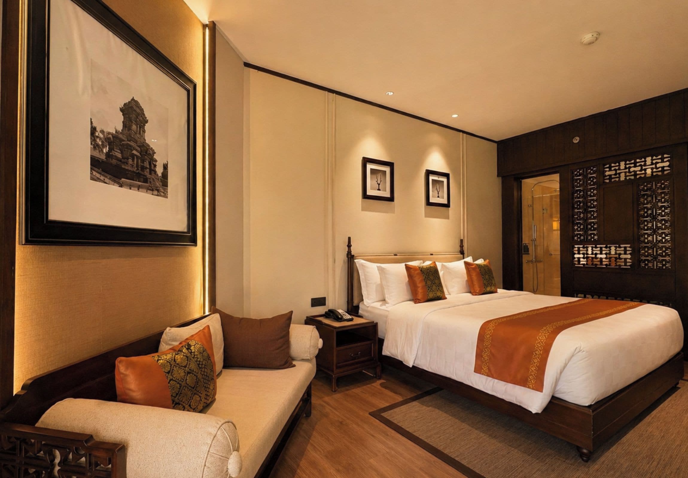A hotel room with a large bed, a sofa, a nightstand, and a wall-mounted TV.