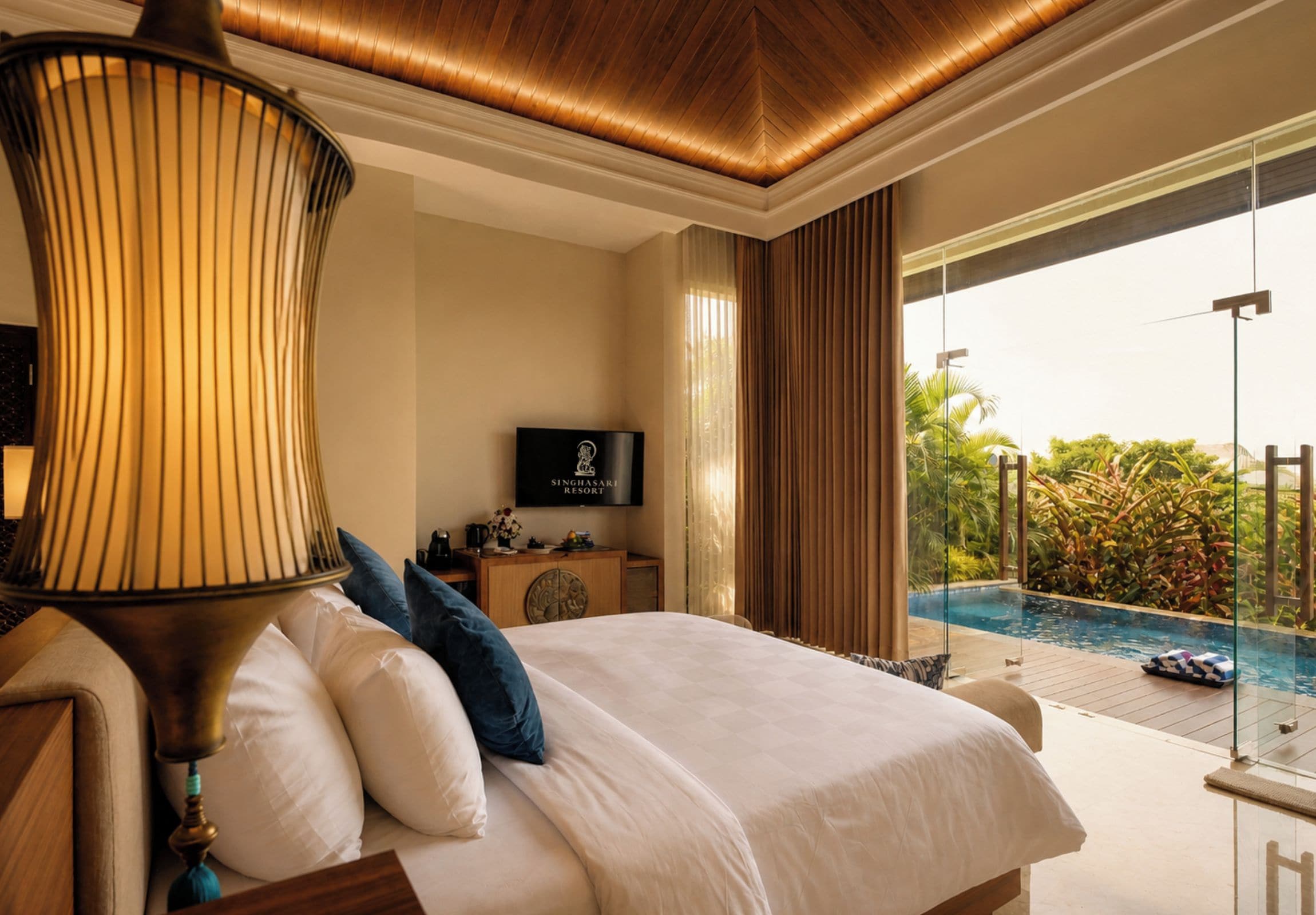 Una habitación de hotel con una cama, televisor, escritorio y vista a una piscina al aire libre.