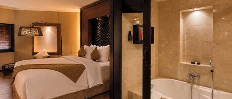 Una habitación de hotel con cama, baño con bañera y espejo montado en la pared.