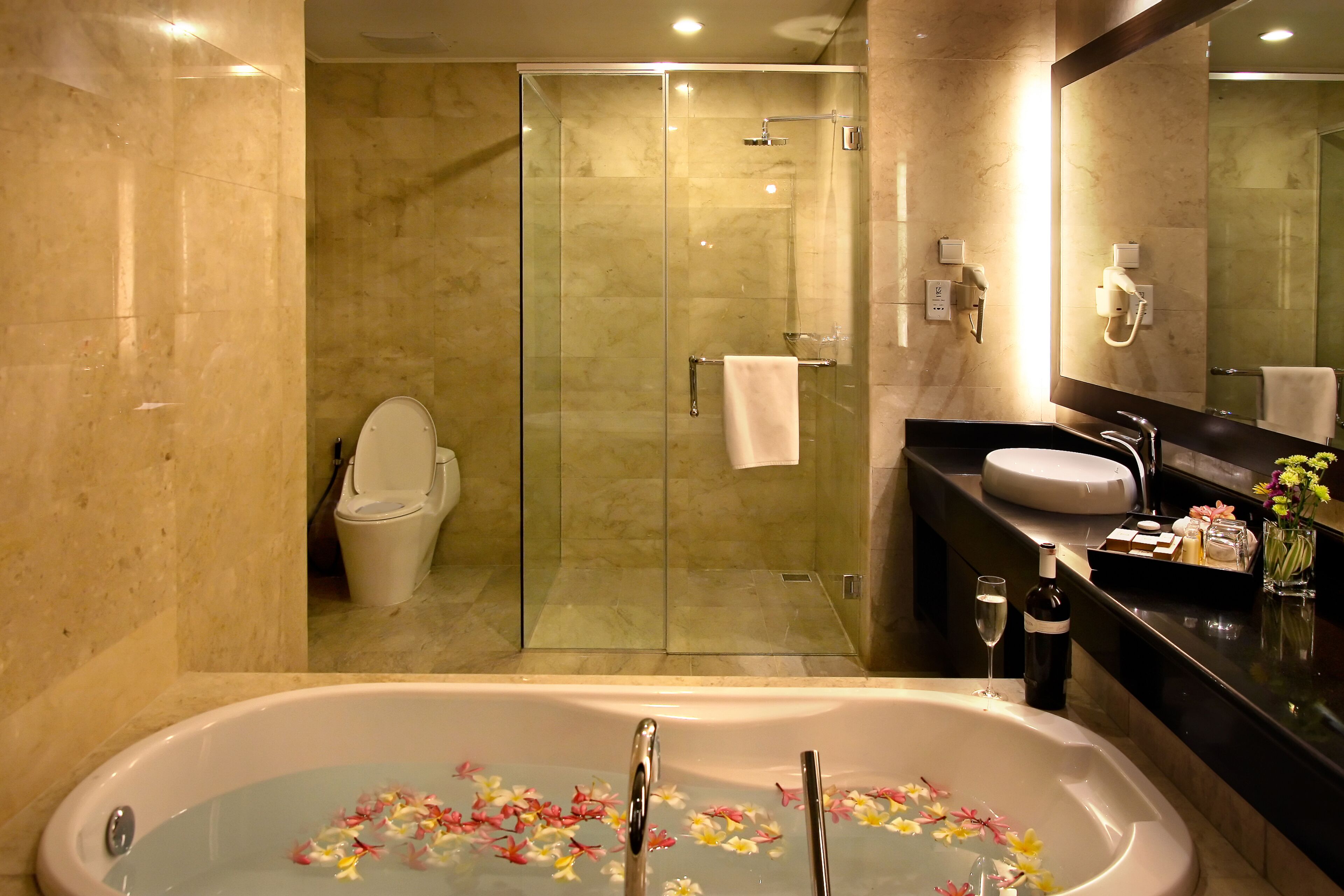 Ein modernes Badezimmer mit einer gläsernen Duschkabine, einer freistehenden Badewanne mit floralen Verzierungen, einem Waschtisch mit Spiegel und einer Toilette.