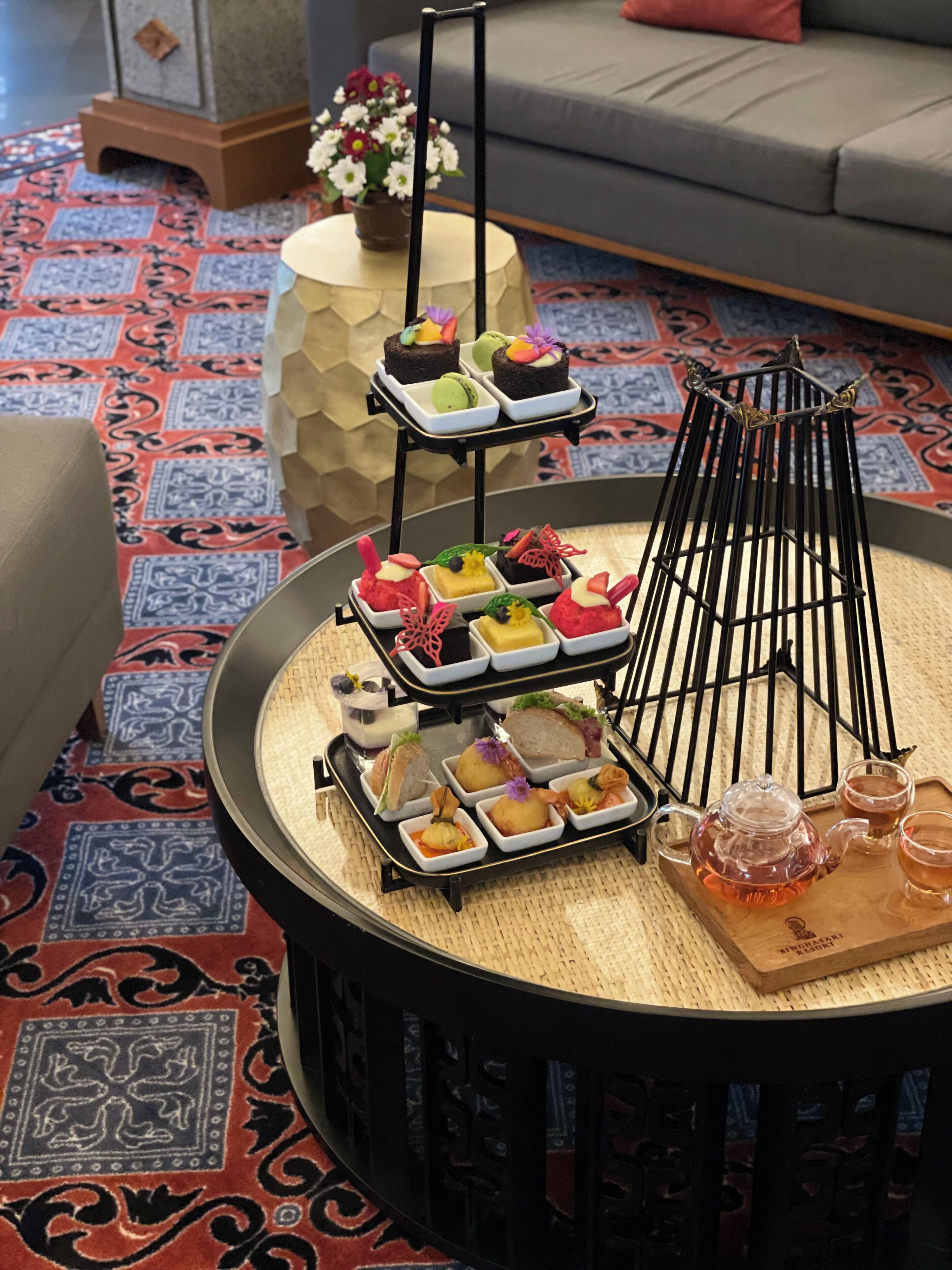 A round coffee table with a tiered dessert stand, a teapot, and two cups on a patterned rug.
