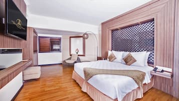 Una habitación de hotel amplia con una cama grande, un televisor de pantalla plana en la pared, una zona de estar con una silla y una mesita.
