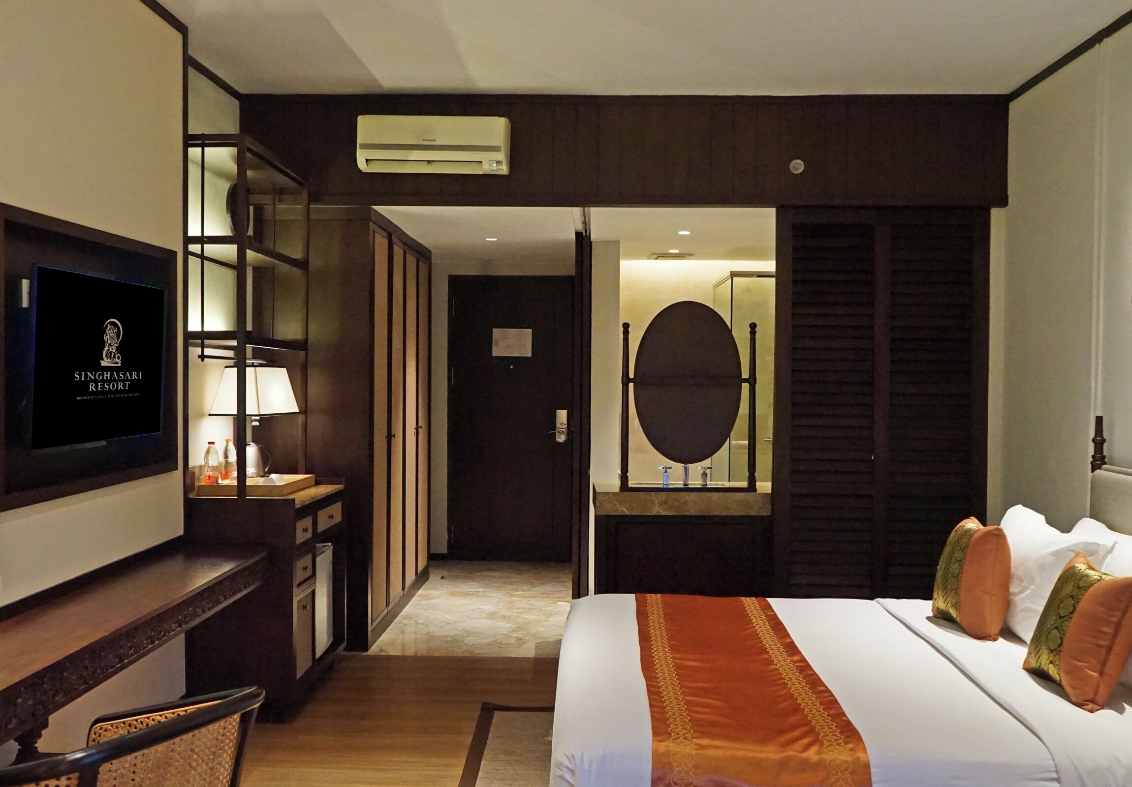 A hotel room with a bed, a TV, a desk, a mirror, and a wardrobe.