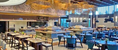 A spacious dining area with multiple tables and chairs, a central bar, and a high ceiling with a grid pattern.