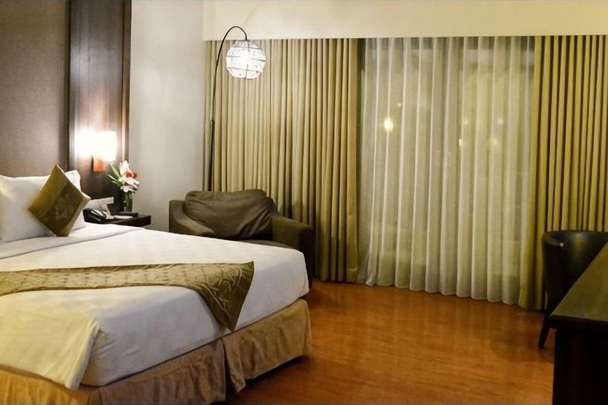 A hotel room with a bed, a chair, a desk, and a large window with curtains.