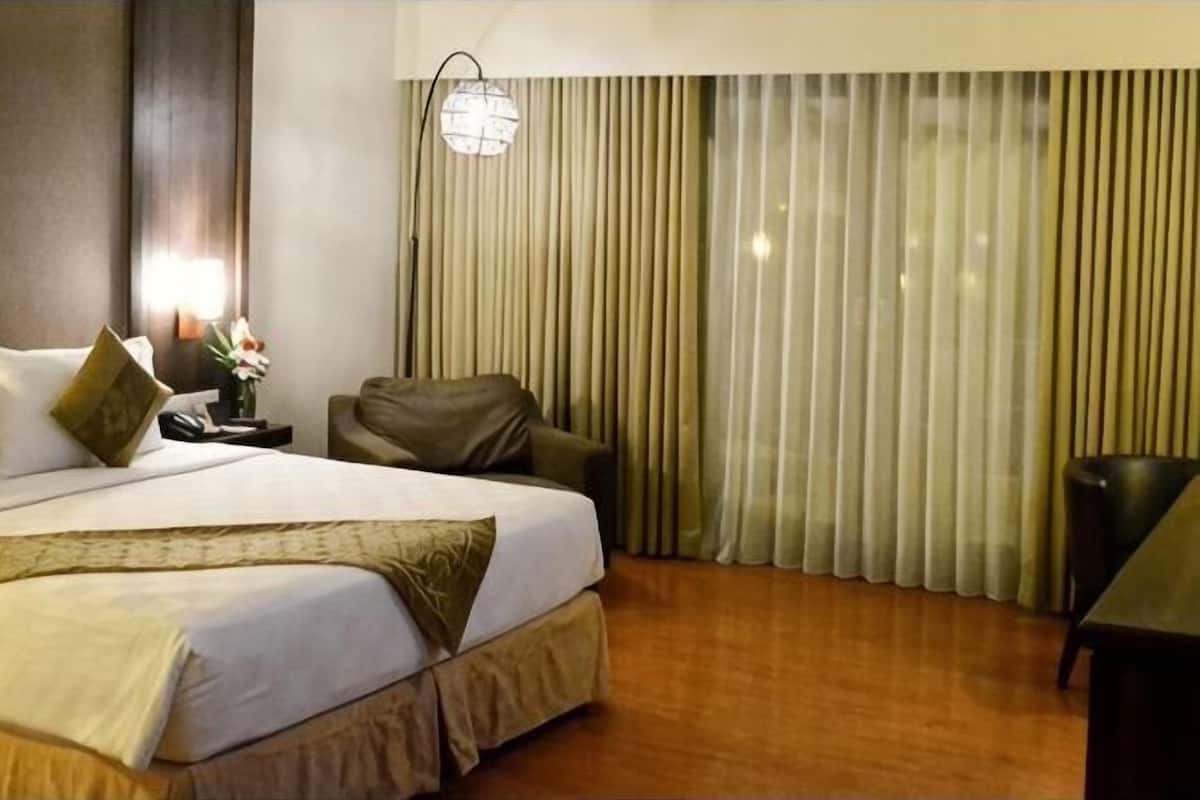 Ein Hotelzimmer mit einem Bett, einem Sessel, einem Schreibtisch und einem großen Fenster mit Vorhängen.