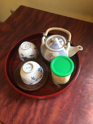 A wooden table with a tray holding a teapot, a teacup, and a container with a green lid. - Kasuga Ryokan (Hiroshima)