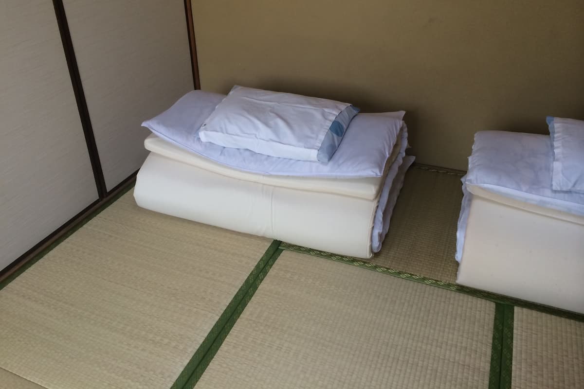 A room with two beds, each with white bedding and pillows, and a tatami mat floor.