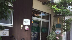 Un ryokan japonés con una bicicleta estacionada afuera, un felpudo y una planta en maceta con flores rosadas.